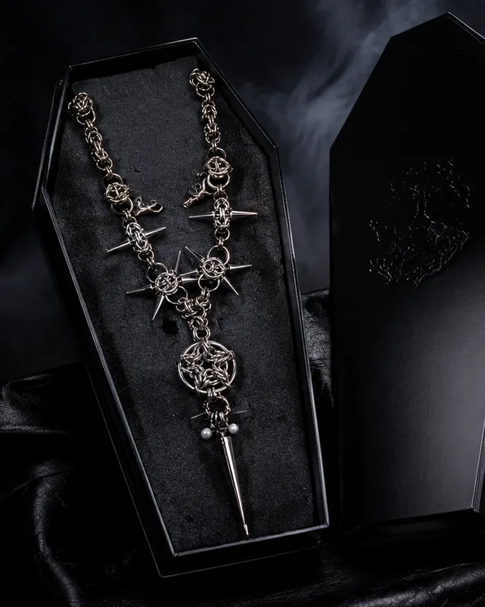 A Grizz Studio® chainmail necklace with spikes resting in an engraved black coffin box
